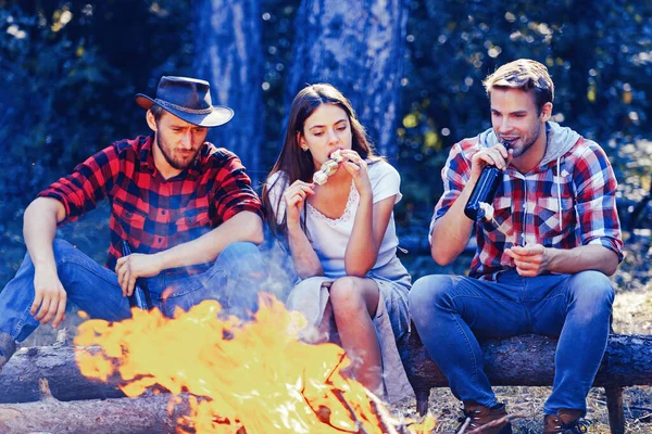 Friends relaxing near campfire after day hiking or gathering mushrooms. Tourism concept. Best friends spend leisure weekend hike barbecue forest nature background.