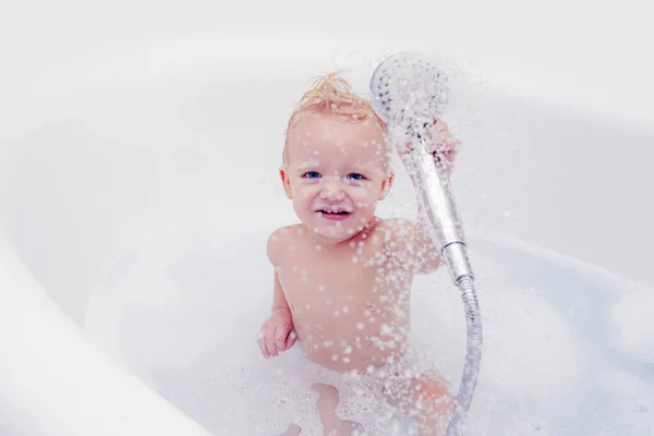 Bébé drôle jouant avec l'eau et la mousse dans un grand évier de cuisine. Petit enfant dans une baignoire . — Photo