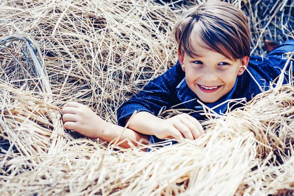 Piccolo bambino carino che tiene foglia d'oro sullo sfondo del villaggio agricolo. Ragazzo sdraiato sul fieno . — Foto Stock