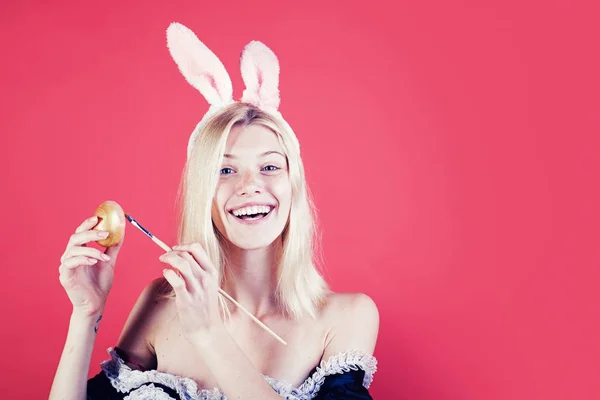 Fröhliche junge Frau bemalt Eier auf rotem Hintergrund. Niedlicher Hase. Attraktive junge Frau mit Hasenohren. Frohe Ostern. — Stockfoto