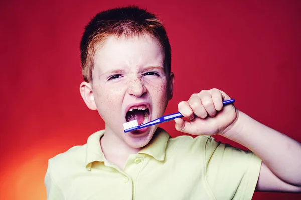 Rapaz sorridente sem um dente com escova de dentes isolada no fundo vermelho. Conceito dentário - menina adolescente sorridente em branco camisa branca escovando os dentes. O rapazinho está a lavar os dentes. . — Fotografia de Stock