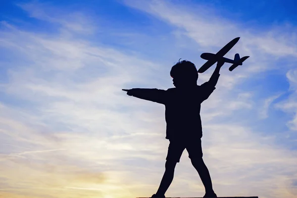 Silhouette of child with airplane in sunlight rays. Concept of dreams and travels. Dreams of flying planes. — Stock Photo, Image