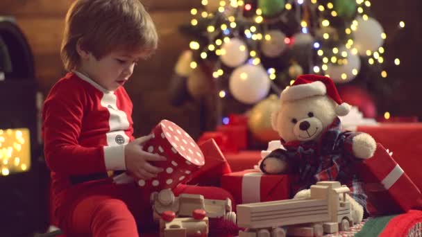 Überraschte süße Kind Mädchen öffnet ein Weihnachtsgeschenk. Weihnachtskind Eröffnungsgeschenk zu Hause. Neues Jahr für süßes Kind. Frohe Weihnachten Kind in Weihnachtsmütze mit Geschenk haben ein Weihnachten. Emotionen schenken.