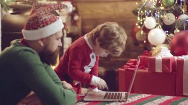 Baba oğul Noel 'de eğleniyorlar. Babası defteri olan sevimli bir oğlu var. Noel ailesi. Mutlu baba ve oğul Noel Baba şapkası takıp Noel 'i kutlayalım..