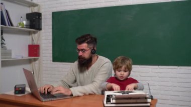 Masasında eski daktilo ve dizüstü bilgisayarı olan bir baba ve oğul. Yaşlılar ve gençler. Teknoloji ilerlemesi.