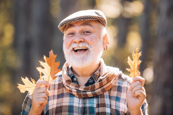 Portrait of a senior man outdoors walking in a park. Autumn and active holidays. Old man alone in autumn park. Senior man hiking in autumn park. — Stock Photo, Image