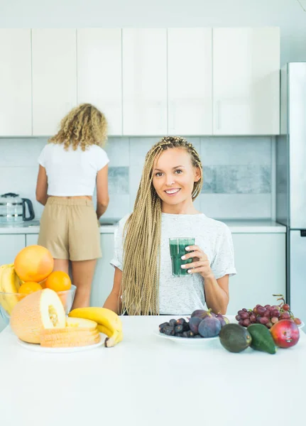 Jovem mulher bebendo smoothie verde na cozinha com frutas e legumes. Mulher bebendo matcha de vidro em casa. Supercomida. Coquetel natural orgânico com amora . — Fotografia de Stock