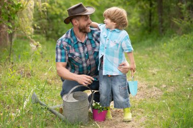 Baba oğul sulama tenekesiyle doğada. Bahçe aletleri. Ağaç dikiyorum. Babası küçük oğluna bitkileri yetiştirmeyi öğretiyor. Bahçedeki küçük yardımcı. Gezegeni daha yeşil yap. Bitki yetiştiriyorum. Bitkilerle ilgilen..