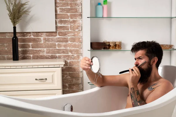 Handsome bearded man washing in bath. Grooming beard. Bearded man with beard with mirror in hand. Morning hygiene. — Stock Photo, Image