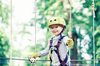 Mutlu çocuk çocuk yüksek ağaç ve halatlar tırmanırken arıyor. Ağaçların arasında bir ip parkta güzel bir çocuk portresi. Küçük çocuk çocukluk yıllarını zevk.