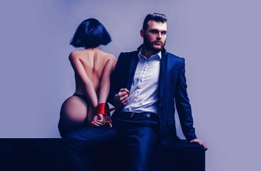 Cinsel ilişkiler. Seks oyunu. Dalga geç ve baştan. Seksi kız çıplak kalça. Tutkulu aşıklar. Seks hakimiyeti. Seks teslimiyeti. Maço bakımlı hipster ve çıplak seksi kadın elleri kırmızı kurdele bağlı
