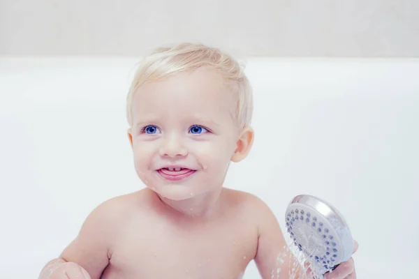 Vicces aranyos baba az úszás, a hab a fürdőben. Aranyos kis baba fiú véve fürdő hab és a kacsa játékok egy fehér napos fürdőszoba játszó. — Stock Fotó