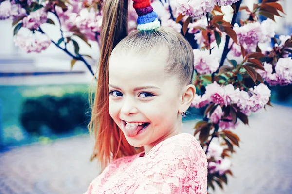 Doğada dilini gösteren neşeli küçük bir kız. Bahar Büyüsü. Bahçe ağacı çiçekleri. Boş zaman. Neşeli mutlu bir çocukluk. — Stok fotoğraf