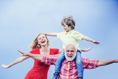 Bearded grandfather and grandson with mother playing with on sunny day. Grandson sits on the shoulders of his grandfather. Grandfather and grandchild.