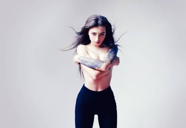 Uzun ince bayan. Uzun saçlı, dövmeli, şehvetli bir model. Moda konsepti. Rüzgarlı saç stili. Çekici bir manken. Vogue ve moda. Çok güzel bir kadın. Üstsüz modeller yüksek bel pantolon giyer.