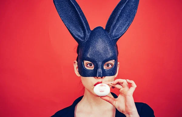 Jovencita pascua, mujer con orejas de conejo. Huella de labio rojo en huevo de Pascua sobre fondo rojo. Impresión de labios rojos. Máscara de conejo mujer . — Foto de Stock