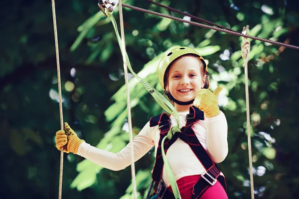 Rope park - climbing center. Artworks depict games at eco resort which includes flying fox or spider net. Hiking in the rope park girl in safety equipment. Roping park. Child. — Stock Photo, Image