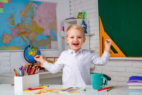 Gelukkige jongen in het klaslokaal vlakbij schoolbord bureau. Grappige schoolkinderen bij de les. Portret van leerlingen van het basisonderwijs binnenshuis. — Stockfoto