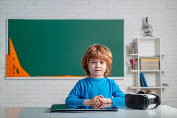 Individuele bijles. Vriendelijk kind in de klas vlakbij schoolbord bureau. Kleine jongen die speelt met digitale tablet. Schoolkind met tablet in klaslokaal. — Stockfoto