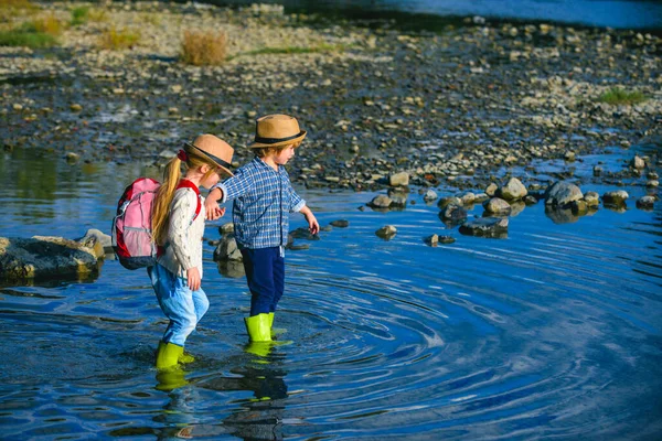 Amitié et soutien. Enfants avec des sacs à dos de voyage sur la rivière en été. Deux enfants dans une rivière jouant avec l'eau par une chaude journée d'été. Amusement et aventure en plein air pour les enfants . — Photo
