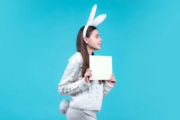 Dziewczyna w stroju Easter Bunny trzymać kartkę na niebieskim tle izolowane. — Zdjęcie stockowe