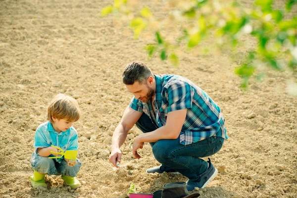 Küçük oğlu ona yardım ederken mutlu, genç bir baba ağaç dikiyor. Baba ve oğul bahçede bahçıvanlık yapıyor.. — Stok fotoğraf