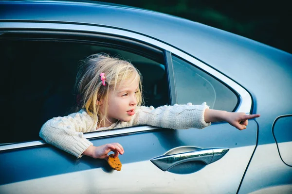 Arabadaki küçük kız bir şey gösteriyor. Arabada oturan küçük kız. Arabasının camından bakan sevimli küçük kız.. — Stok fotoğraf