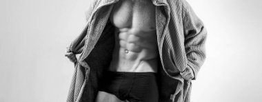 Güçlü atletik adam. Fitness modeli, mükemmel kas gövdesini gri arka planda fotokopi alanı ile izole edilmiş olarak gösteriyor. Kaslı model genç adam bornozunu çıkarıyor..