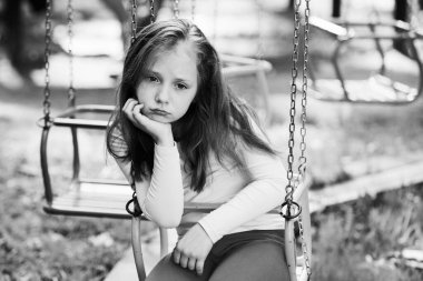 Kız salıncakta sallanıyor. Parkta sıkılmış bir çocuk. Çocuklar için sağlıklı bir yaz aktivitesi. Yazın açık hava aktivitesi.