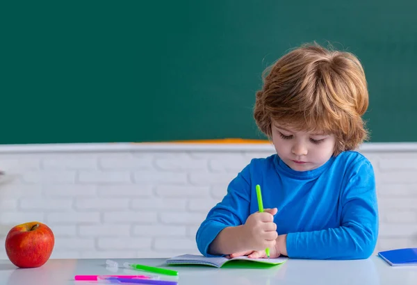 Kleine kinderen op school. Gelukkig schattig ijverig kind zit binnen aan een bureau. Thuisschool voor leerling. Beetje klaar om te studeren. — Stockfoto