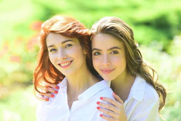 公園に立っている二人の若い幸せな女性の友人。カメラを見て。白いシャツを着た若い女性たちが緑の畑を歩いている。親友だ. — ストック写真