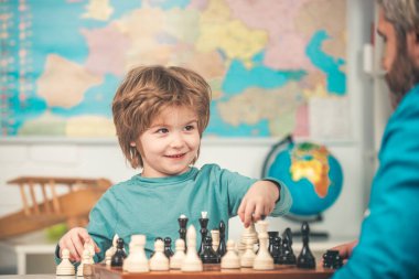 Neşeli gülümseyen küçük çocuk masada oturuyor ve satranç oynarken keyifli bir akşam geçiriyor. Satranç oynarken akıllı konsantre ve düşünen bir çocuk. Eğitim ve insanlar kavramı.
