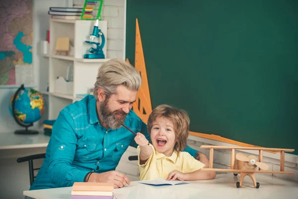 Father teaching son. Home study. Little boy pupil with happy face expression near desk with school supplies. Teacher and pupil in classroom. Elementary school classroom.