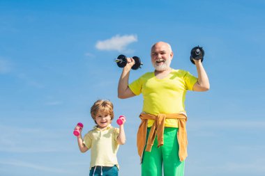 Mavi arka planda izole edilmiş dambıllı kıdemli fitness adamı eğitimi. Yaşlılık sağlığını gevşetmek için bir bahane değildir. Büyükbaba ve çocuk ağırlık kaldırıyor..