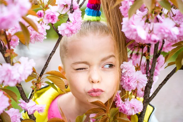 Wiosenna nastolatka w pachnących różowych kwiatach w letnim parku kwiatowym. Komiczny grymas, śmieszne emocje, szalony wytrysk na twarz. — Zdjęcie stockowe