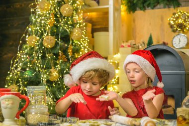 Eğlenceli tatil fırıncıları. Noel Baba için zencefilli kurabiye, Noel ışığı arka planına karşı. Komik çocuklar Noel Baba için kurabiye yapıyor..