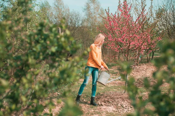 Happy young woman gardener spraying water on plants. Hobby concept. Girl gardening on spring garden. — Stock Photo, Image