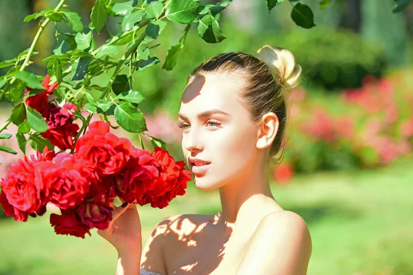 Ragazza carina con fiore in piedi nel campo di rose, all'aperto. Stagione primaverile . — Foto Stock