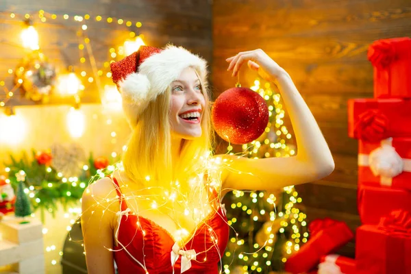 Mulher de Natal sorridente com lábios vermelhos segurando bola de Natal, bugiganga vermelha. A rapariga está a usar chapéu de Pai Natal. Conceito de férias. Férias de inverno . — Fotografia de Stock