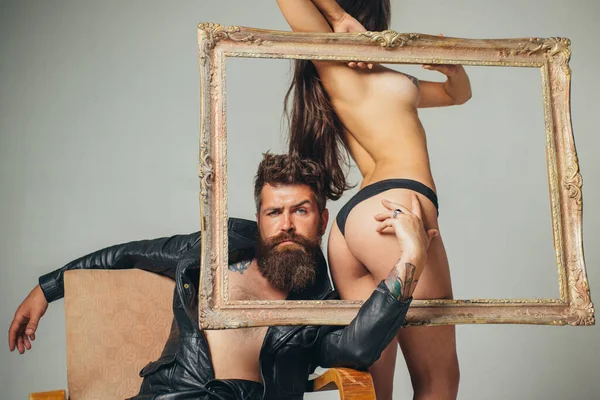 Beautiful young couple through frame. Lady standing behind wooden picture frame.Beautiful female body in black lingerie with muscular man. Sensual. Women Sexy Lingerie. Close up photo. — Stock fotografie