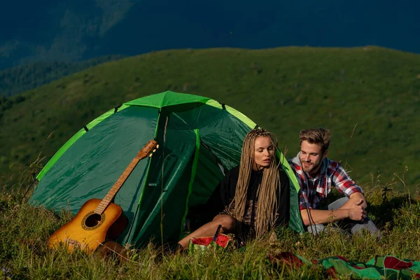 Acampar. Feliz hombre y mujer sonriendo y tocando canciones en la guitarra mientras acampan en las montañas . — Foto de Stock