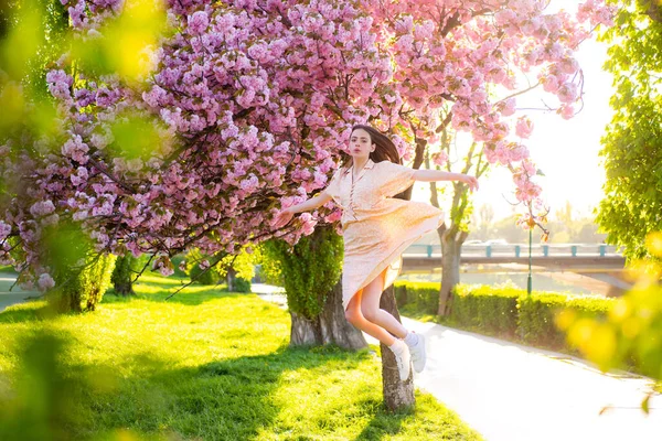Chica saltando en el parque de flores de cerezo rosa. Vacaciones con chica en Sakura. Chica y Sakura. Hermosa mujer joven disfrutando de un día soleado en el parque durante la temporada de flores de cerezo en un bonito día de primavera . — Foto de Stock