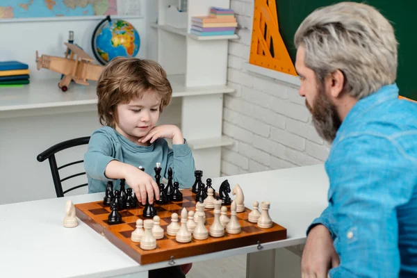 Kleine slimme jongen die aan schaken denkt. Spelen en activiteiten voor kinderen. Vader en zoon ontspannen samen. Leraar en kind. — Stockfoto