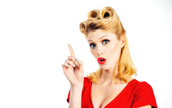 Portrait of beautiful young surprised woman, dressed in red pin-up dress. Caucasian blond model posing in retro fashion concept. Looking camera, showing pointing, copyspace. Thinking, daydreaming. — Stock Photo, Image