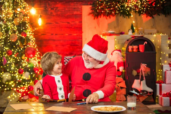 Criança ajudante de Natal escrevendo carta para a carta do Papai Noel em chapéu vermelho. Bonito menino escrevendo carta para o Papai Noel em casa . — Fotografia de Stock