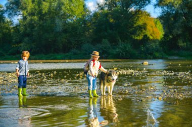 Dağlarda yürüyüş yapan çocuklar nehri geçiyorlar. Çocuklar dağda suda oynarlar. Bahar tatili. Yürüyüş yolunda küçük bir oğlan ve kız. Açık hava eğlencesi. Çocuklarla aktif bir eğlence. Komik çocuklar oynuyor.