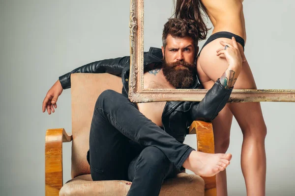 Bare hot girl with sexy ass standing behind a frame. Handsome muscular bearded man holding frame with sexy hot woman. Abstract art. Sexy couple isolated at grey background. — 스톡 사진