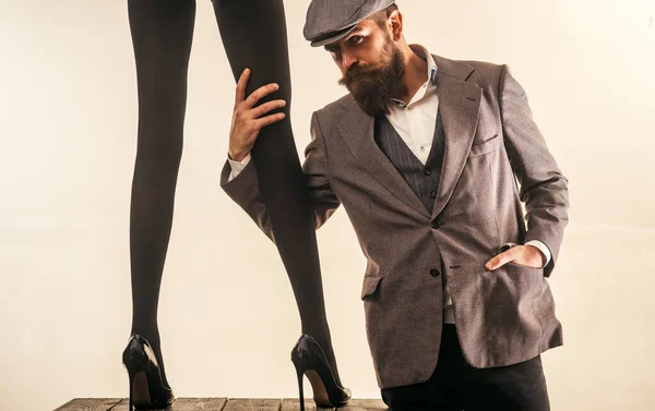 Handsome bearded apparel cutter designer man taking measurements from sexy hot beautiful girl. Long sexy woman legs in black tights. Atelier worker flirting with female. — Stock Photo, Image