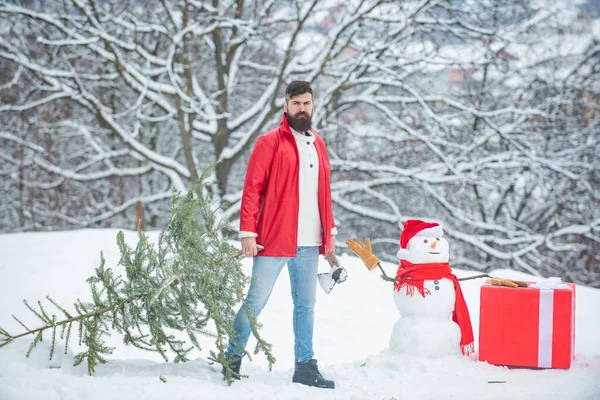 Hipster Waldarbeiter mit Weihnachtsbaum. Holzfäller mit Axt im Winterwald. Bärtiger Mann mit frisch gefälltem Weihnachtsbaum im Wald. — Stockfoto