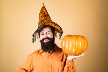 Şeytan adam. Cadılar Bayramı şapkalı yakışıklı adam balkabağı tutuyor. Yakından bir portre. Cadılar Bayramı Adamı balkabağıyla poz veriyor. Cadılar Bayramı afişi için tasarım. Mutlu Cadılar Bayramı Etiketleri.